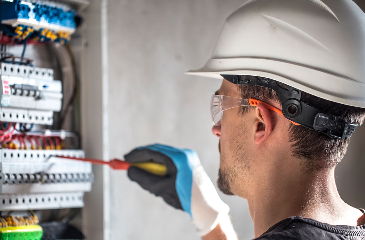 électricien avec casque et lunettes de protection travaillant sur un tableau électrique